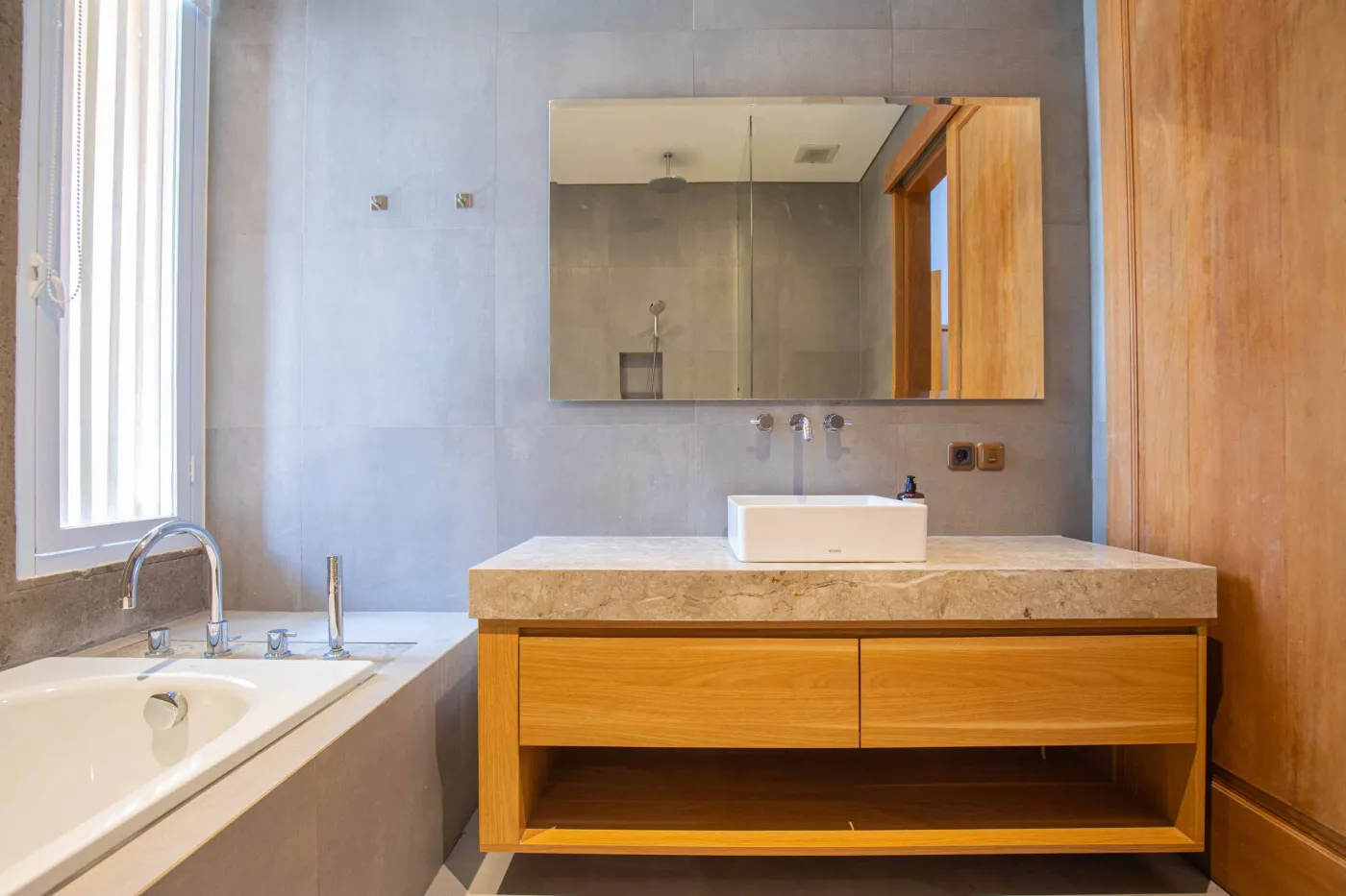 Modern minimalist kitchen with light wood cabinets, granite counters, sink, stovetop, microwave, and open dining area against a concrete wall. - Bali Villas