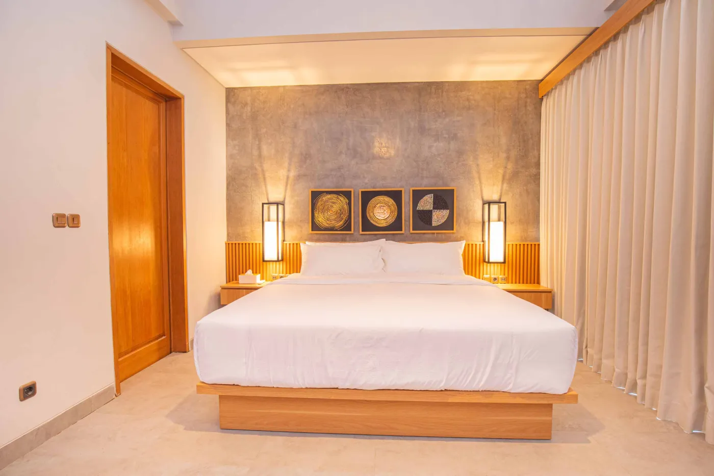 Modern minimalist kitchen with light wood cabinets, granite counters, sink, stovetop, microwave, and open dining area against a concrete wall. - Bali Villas