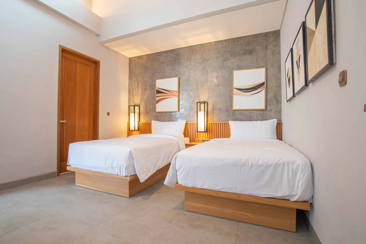 Modern minimalist kitchen with light wood cabinets, granite counters, sink, stovetop, microwave, and open dining area against a concrete wall. - Bali Villas