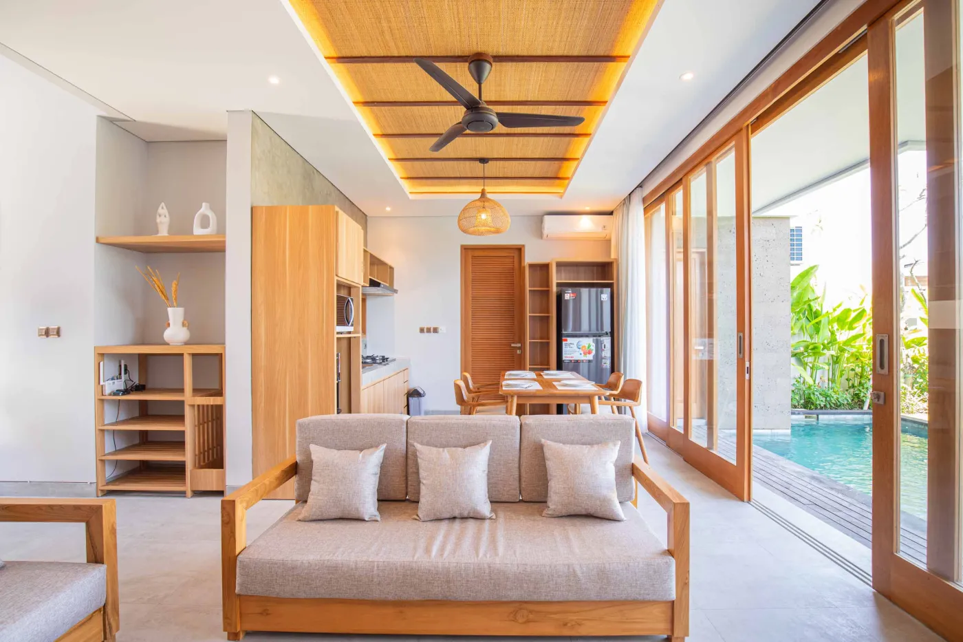 Modern minimalist kitchen with light wood cabinets, granite counters, sink, stovetop, microwave, and open dining area against a concrete wall. - Bali Villas