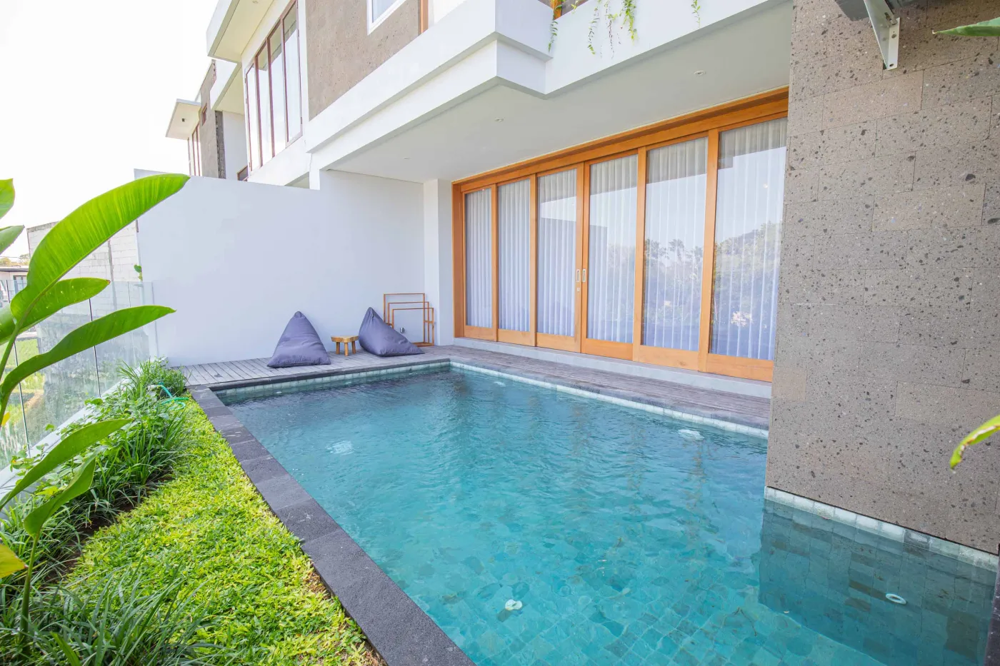 Serene turquoise private pool in a lush tropical garden beside a modern Balinese villa with wooden accents and floor cushions. - Bali Villas