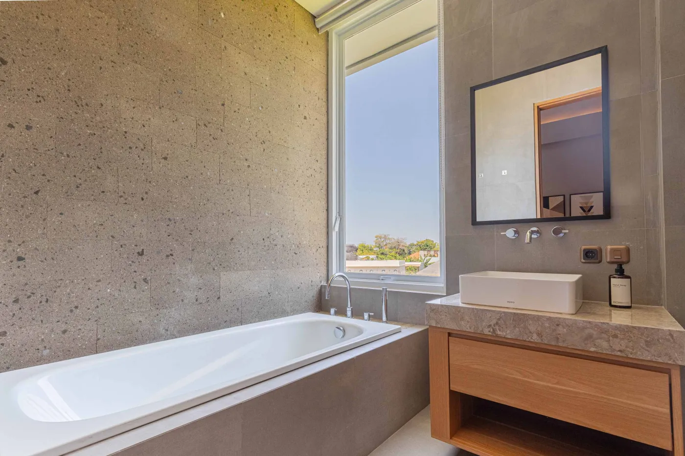 Modern minimalist kitchen with light wood cabinets, granite counters, sink, stovetop, microwave, and open dining area against a concrete wall. - Bali Villas