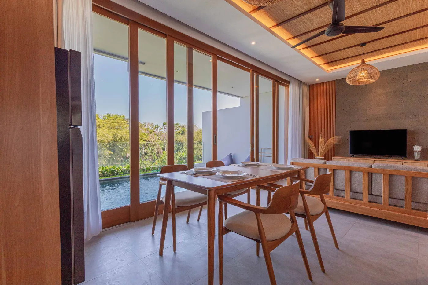 Modern minimalist kitchen with light wood cabinets, granite counters, sink, stovetop, microwave, and open dining area against a concrete wall. - Bali Villas