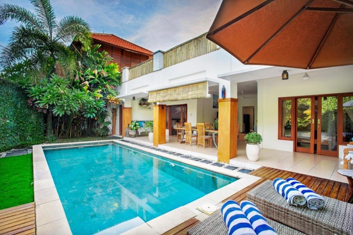 Luxurious Bali villa with infinity pool, tropical garden, wooden lounge chairs, and outdoor dining area. - Bali Villas