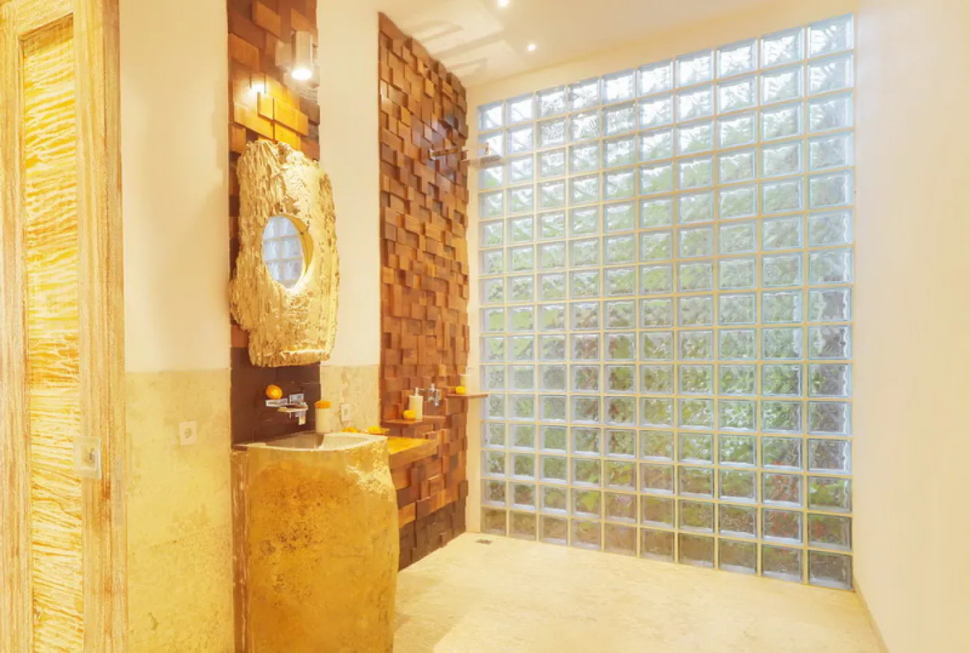 Modern luxury bathroom featuring a frosted glass block window, wooden accent wall with rain showerhead, and fresh flowers on a side table. - Bali Villas
