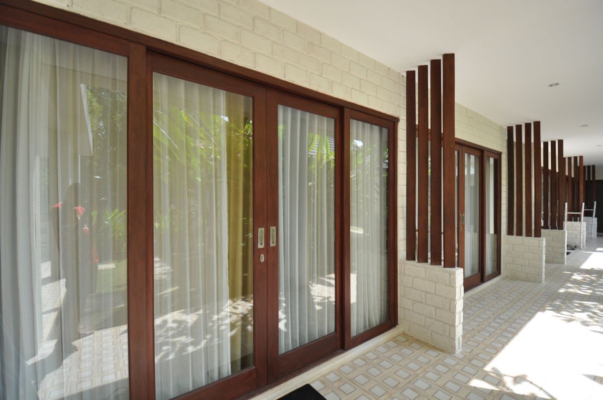 Reception at The Lokale Residences in Bali: smiling Balinese staff in traditional attire greets visitors behind wooden desk amid tropical plants and open courtyard. - Bali Villas