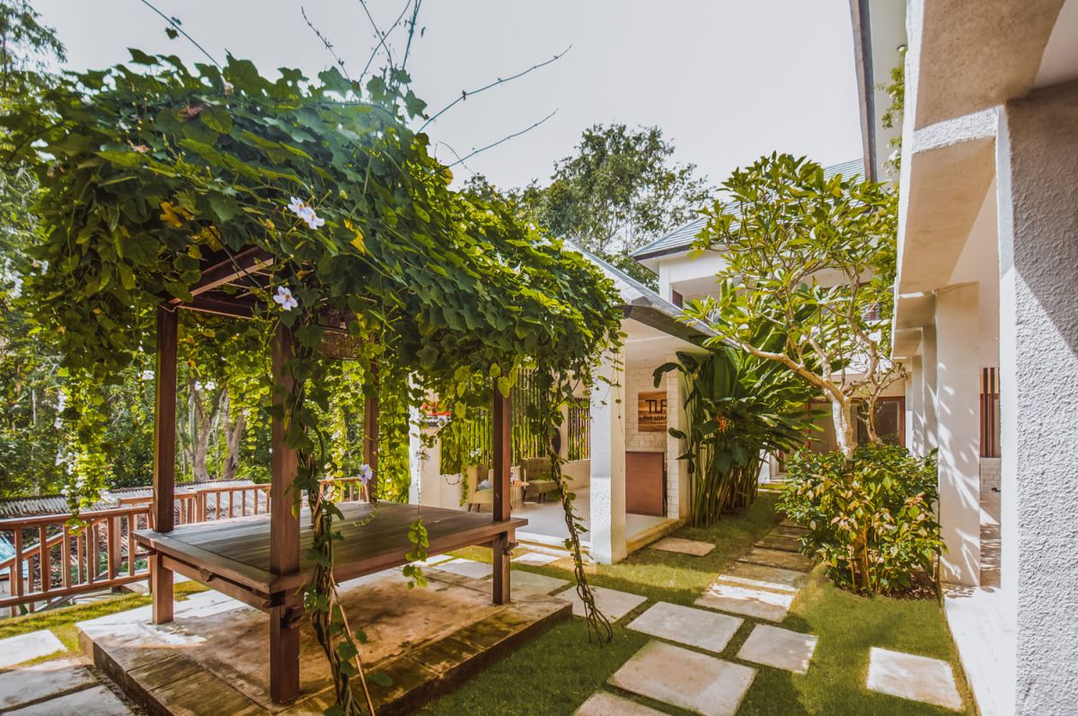Reception at The Lokale Residences in Bali: smiling Balinese staff in traditional attire greets visitors behind wooden desk amid tropical plants and open courtyard. - Bali Villas