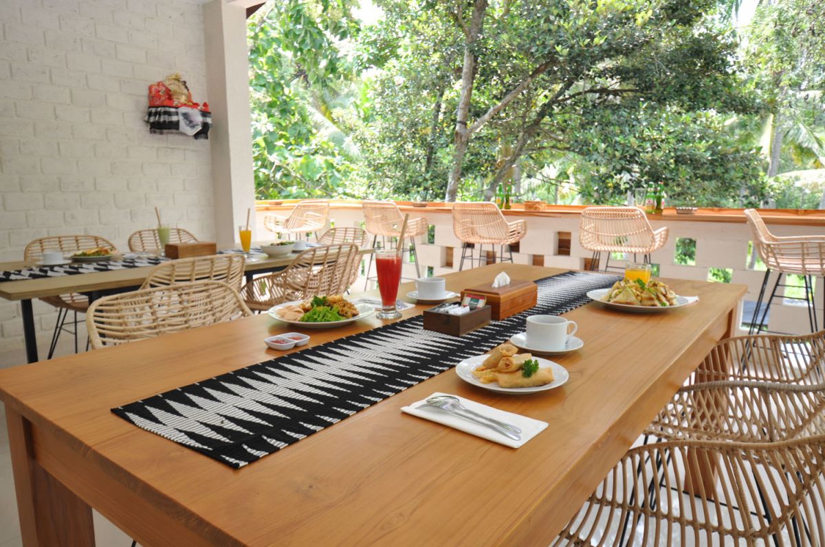 Reception at The Lokale Residences in Bali: smiling Balinese staff in traditional attire greets visitors behind wooden desk amid tropical plants and open courtyard. - Bali Villas