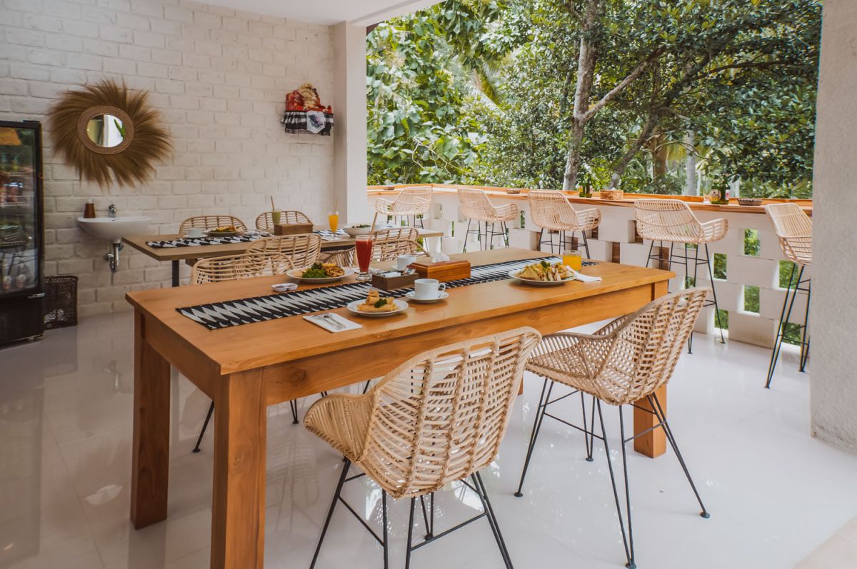 Reception at The Lokale Residences in Bali: smiling Balinese staff in traditional attire greets visitors behind wooden desk amid tropical plants and open courtyard. - Bali Villas