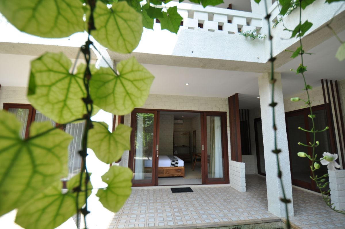Reception at The Lokale Residences in Bali: smiling Balinese staff in traditional attire greets visitors behind wooden desk amid tropical plants and open courtyard. - Bali Villas