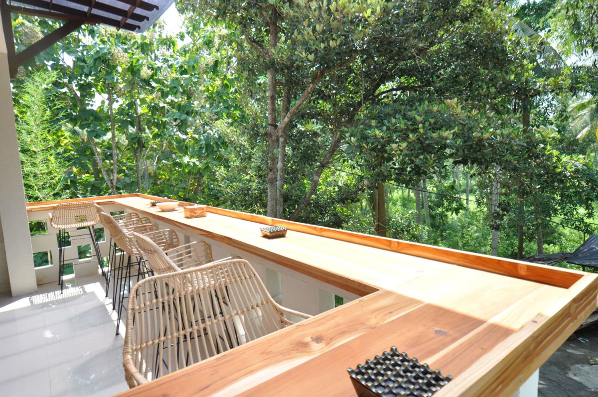 Reception at The Lokale Residences in Bali: smiling Balinese staff in traditional attire greets visitors behind wooden desk amid tropical plants and open courtyard. - Bali Villas