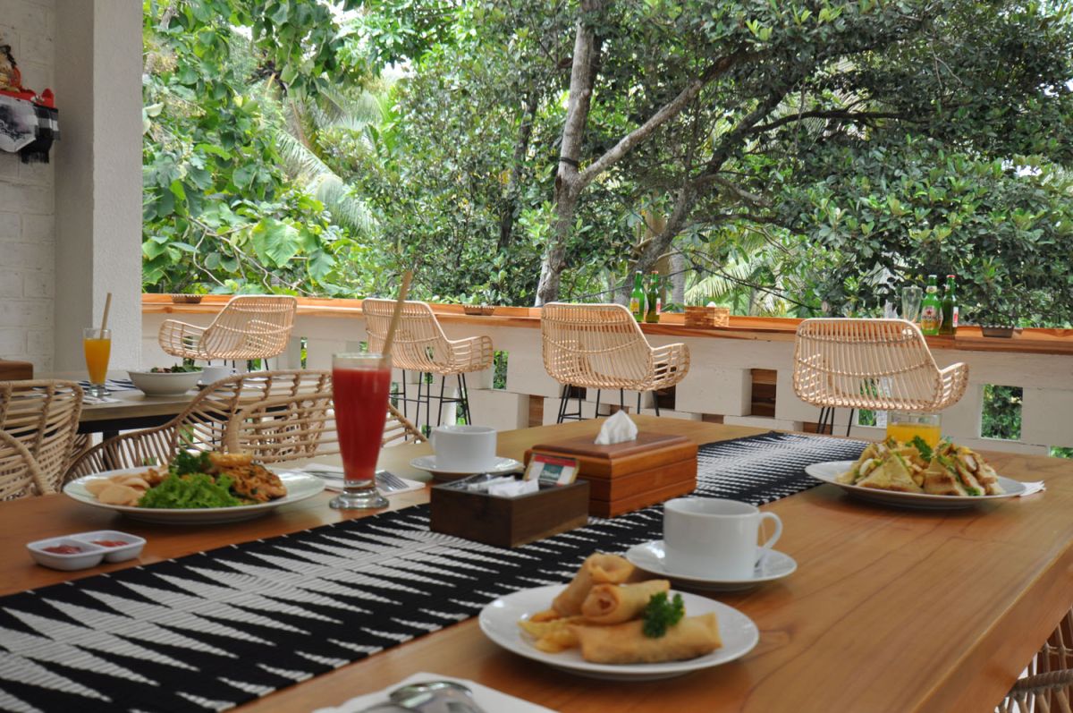Reception at The Lokale Residences in Bali: smiling Balinese staff in traditional attire greets visitors behind wooden desk amid tropical plants and open courtyard. - Bali Villas