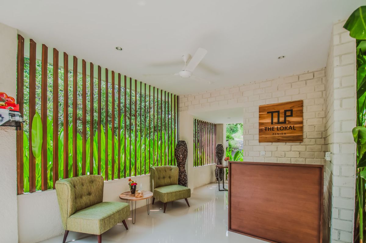 Reception at The Lokale Residences in Bali: smiling Balinese staff in traditional attire greets visitors behind wooden desk amid tropical plants and open courtyard. - Bali Villas