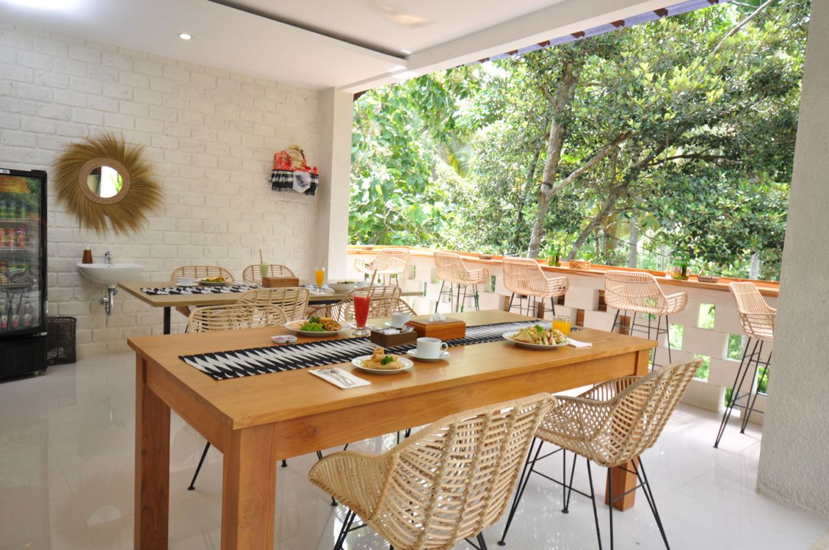 Reception at The Lokale Residences in Bali: smiling Balinese staff in traditional attire greets visitors behind wooden desk amid tropical plants and open courtyard. - Bali Villas