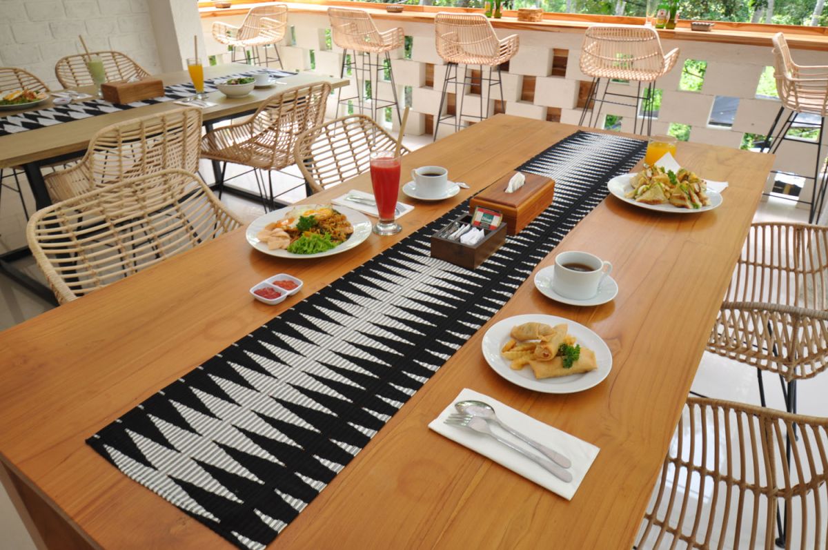 Reception at The Lokale Residences in Bali: smiling Balinese staff in traditional attire greets visitors behind wooden desk amid tropical plants and open courtyard. - Bali Villas