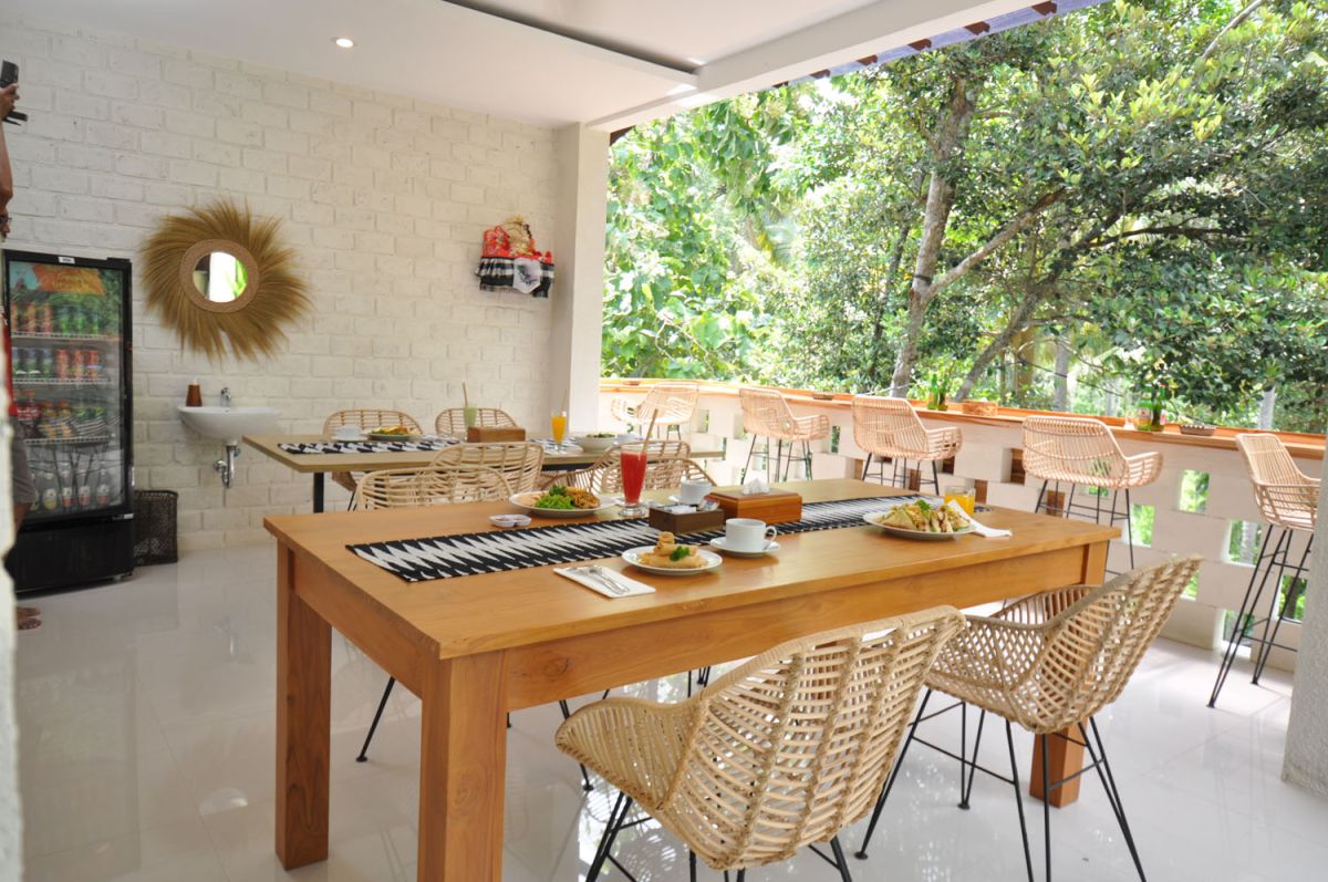 Reception at The Lokale Residences in Bali: smiling Balinese staff in traditional attire greets visitors behind wooden desk amid tropical plants and open courtyard. - Bali Villas