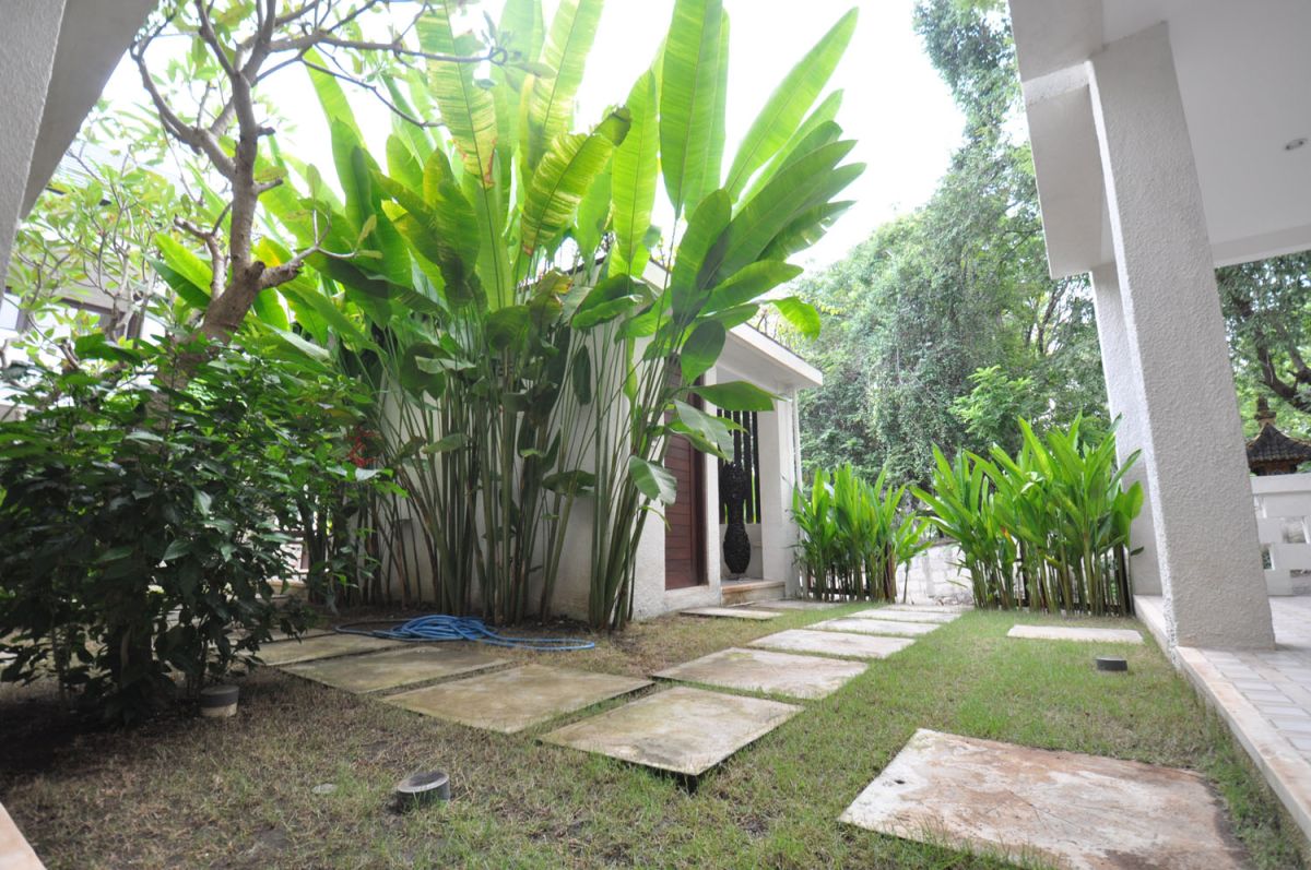 Reception at The Lokale Residences in Bali: smiling Balinese staff in traditional attire greets visitors behind wooden desk amid tropical plants and open courtyard. - Bali Villas