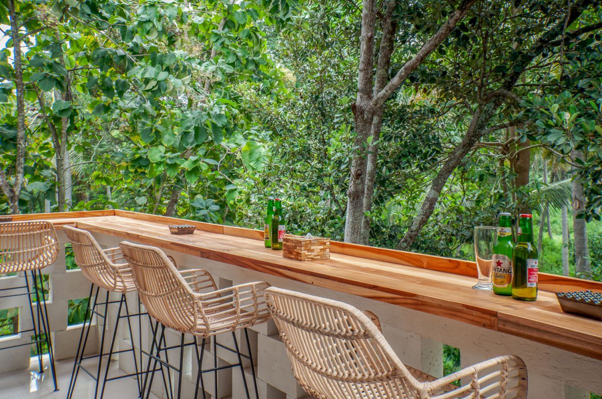 Reception at The Lokale Residences in Bali: smiling Balinese staff in traditional attire greets visitors behind wooden desk amid tropical plants and open courtyard. - Bali Villas