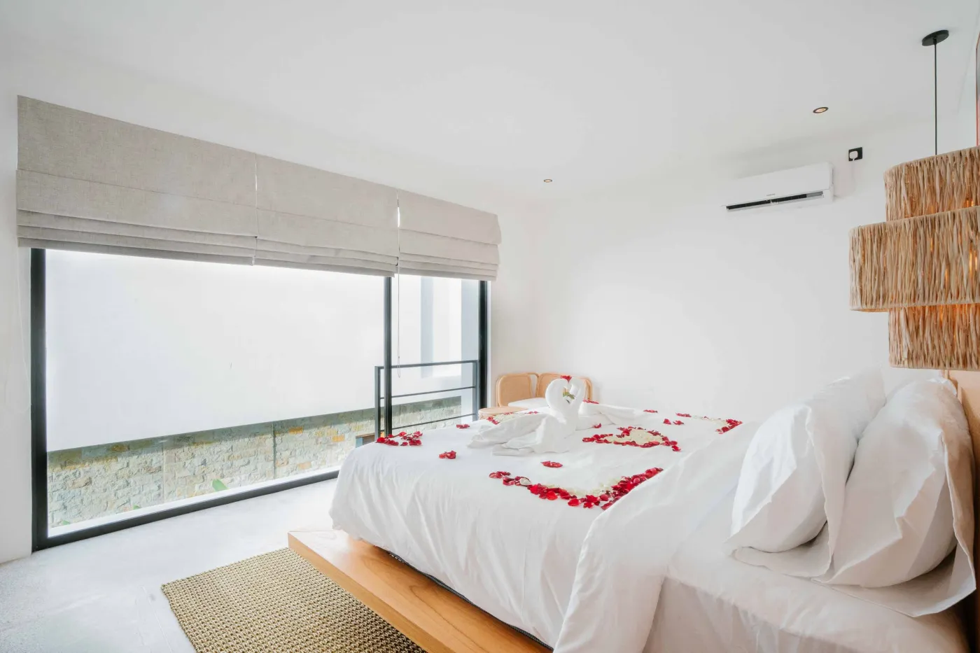 Modern minimalist bathroom interior featuring a walk-in shower, concrete vanity with sink and mirror, rattan pendant lights, and potted pampas grass. - Bali Villas