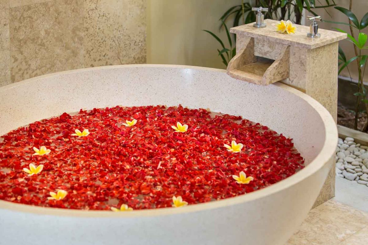 Modern U-shaped kitchen with dark wood cabinets, gold mosaic tile backsplash, granite counters, gas stove, and a bowl of fresh tropical fruits. - Bali Villas