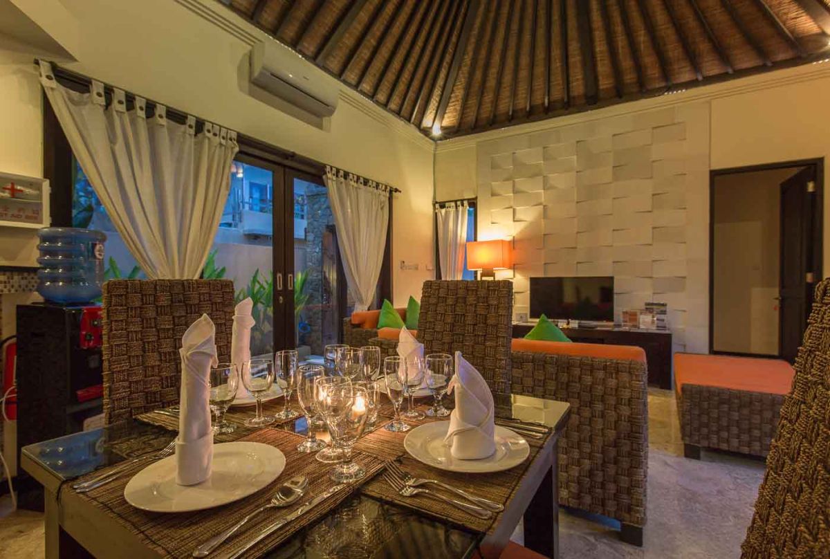 Modern U-shaped kitchen with dark wood cabinets, gold mosaic tile backsplash, granite counters, gas stove, and a bowl of fresh tropical fruits. - Bali Villas