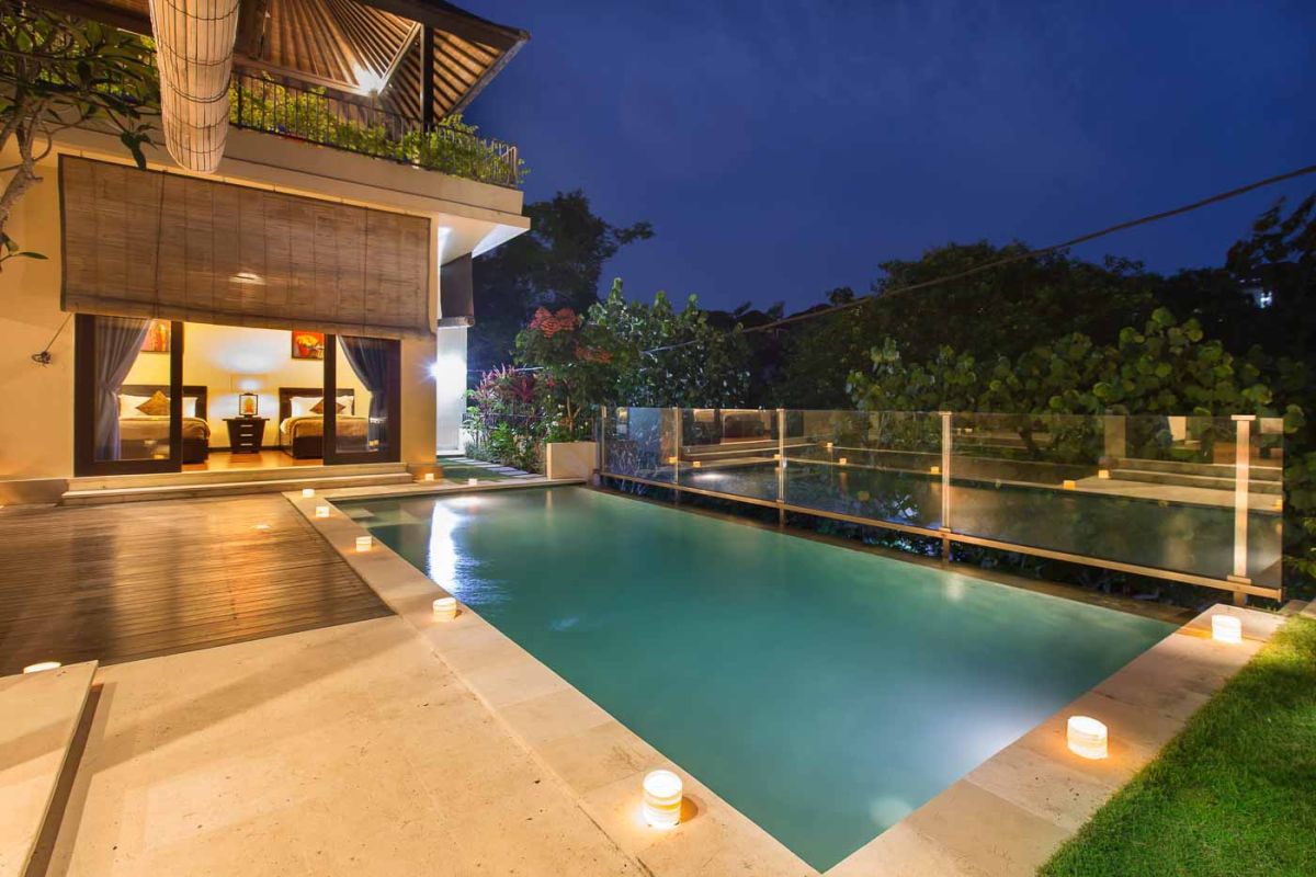 Modern U-shaped kitchen with dark wood cabinets, gold mosaic tile backsplash, granite counters, gas stove, and a bowl of fresh tropical fruits. - Bali Villas