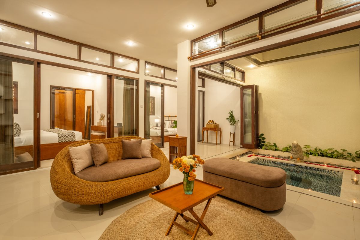 Elegant Balinese-style bathroom with white bathtub filled with red rose petals, wooden carved shutters, wall-mounted shower, and sleek sink. - Bali Villas