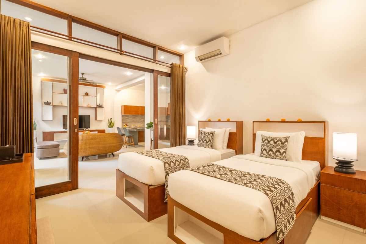 Elegant Balinese-style bathroom with white bathtub filled with red rose petals, wooden carved shutters, wall-mounted shower, and sleek sink. - Bali Villas