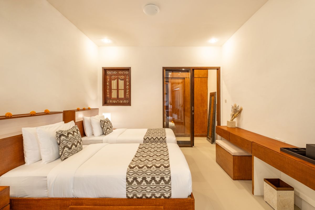 Elegant Balinese-style bathroom with white bathtub filled with red rose petals, wooden carved shutters, wall-mounted shower, and sleek sink. - Bali Villas