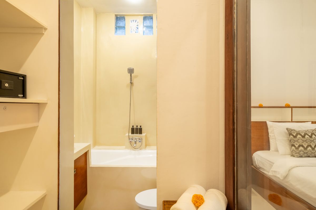 Elegant Balinese-style bathroom with white bathtub filled with red rose petals, wooden carved shutters, wall-mounted shower, and sleek sink. - Bali Villas