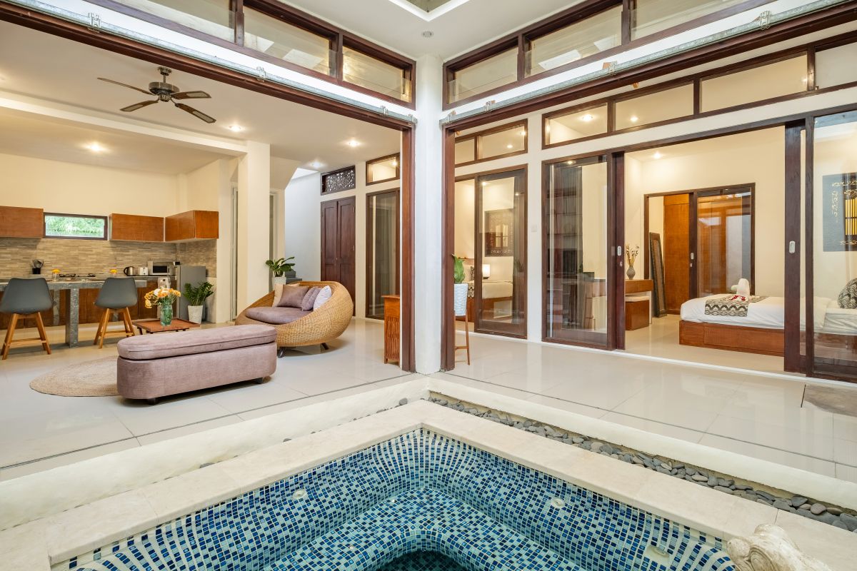 Elegant Balinese-style bathroom with white bathtub filled with red rose petals, wooden carved shutters, wall-mounted shower, and sleek sink. - Bali Villas