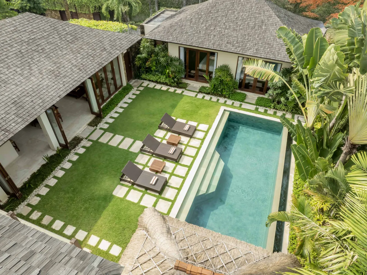 Traditional Balinese thatched pavilion with cushioned daybed in lush tropical garden, lounge chair by small pool. - Bali Villas