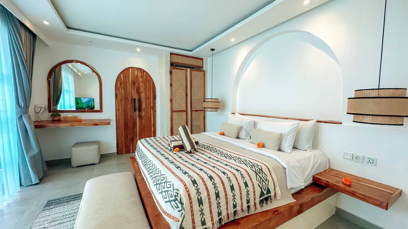 Elegant Balinese villa bedroom with king bed in flower petals spelling "HAPPY", arched wooden doors, bamboo accents, and white walls. - Bali Villas
