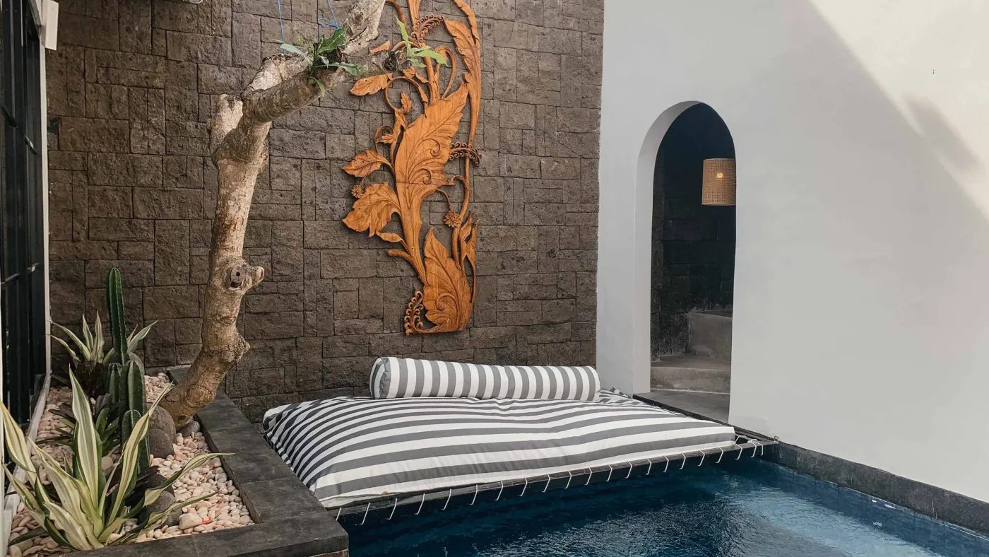 Elegant Balinese villa bedroom with king bed in flower petals spelling "HAPPY", arched wooden doors, bamboo accents, and white walls. - Bali Villas