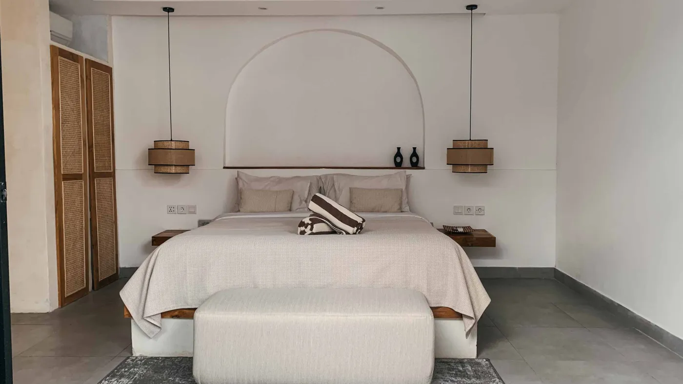 Elegant Balinese villa bedroom with king bed in flower petals spelling "HAPPY", arched wooden doors, bamboo accents, and white walls. - Bali Villas