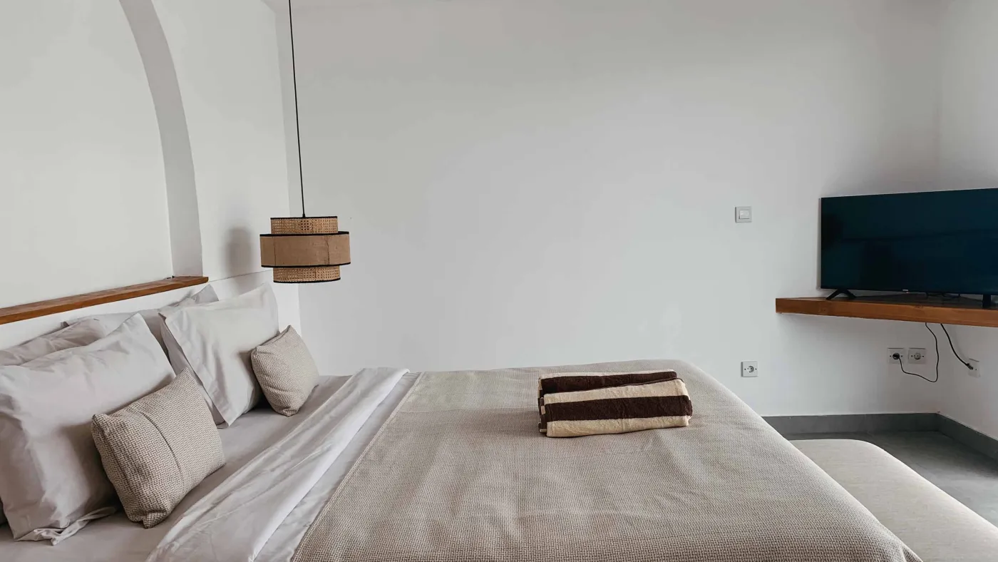 Elegant Balinese villa bedroom with king bed in flower petals spelling "HAPPY", arched wooden doors, bamboo accents, and white walls. - Bali Villas