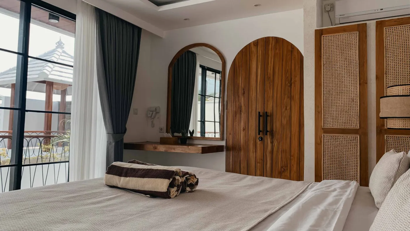 Elegant Balinese villa bedroom with king bed in flower petals spelling "HAPPY", arched wooden doors, bamboo accents, and white walls. - Bali Villas