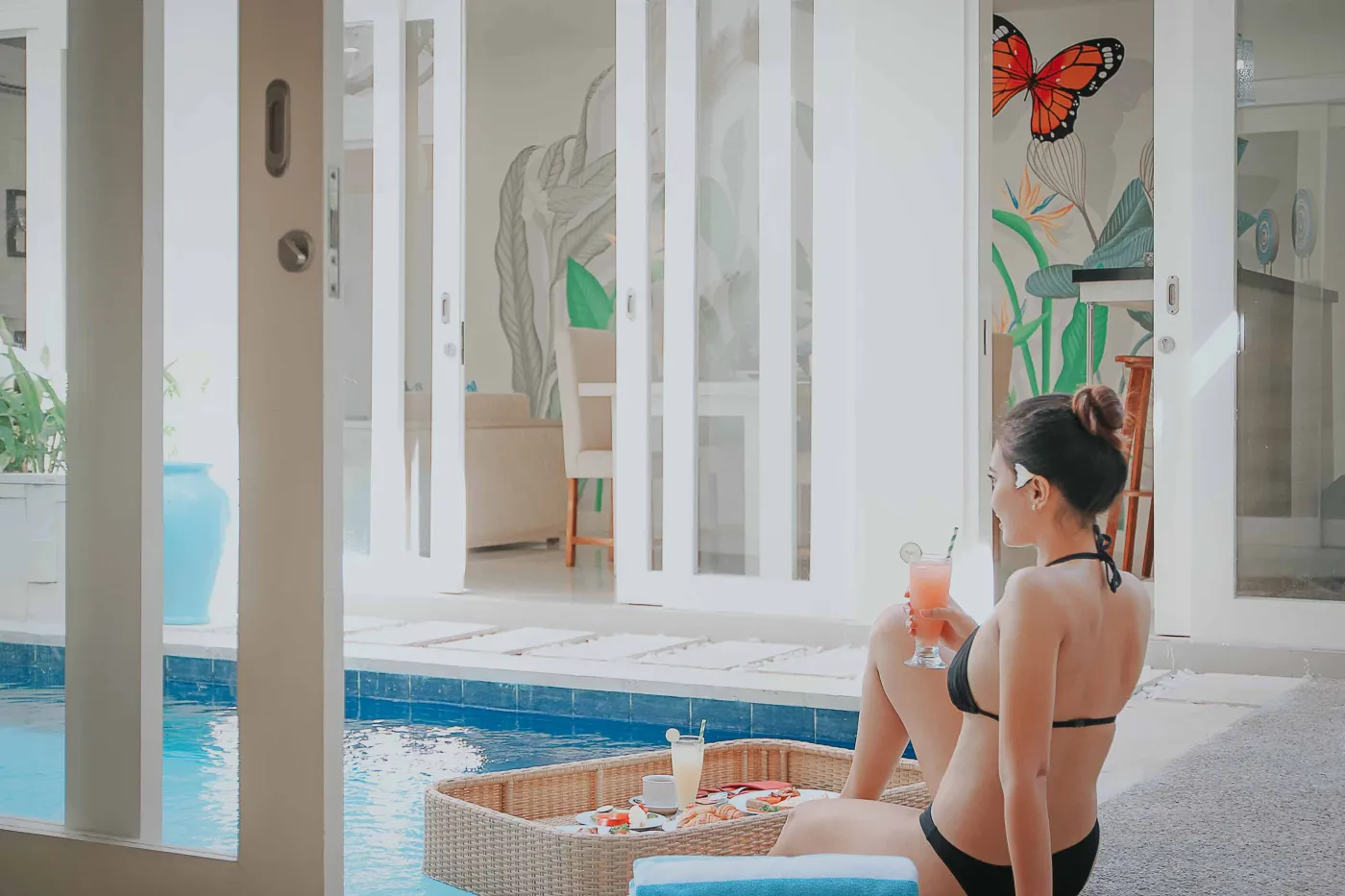 Overhead view of a woman relaxing in a clawfoot bathtub filled with red rose petals, surrounded by tropical plants, Buddha statues, and spa amenities. - Bali Villas