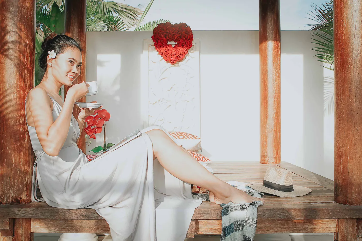 Overhead view of a woman relaxing in a clawfoot bathtub filled with red rose petals, surrounded by tropical plants, Buddha statues, and spa amenities. - Bali Villas