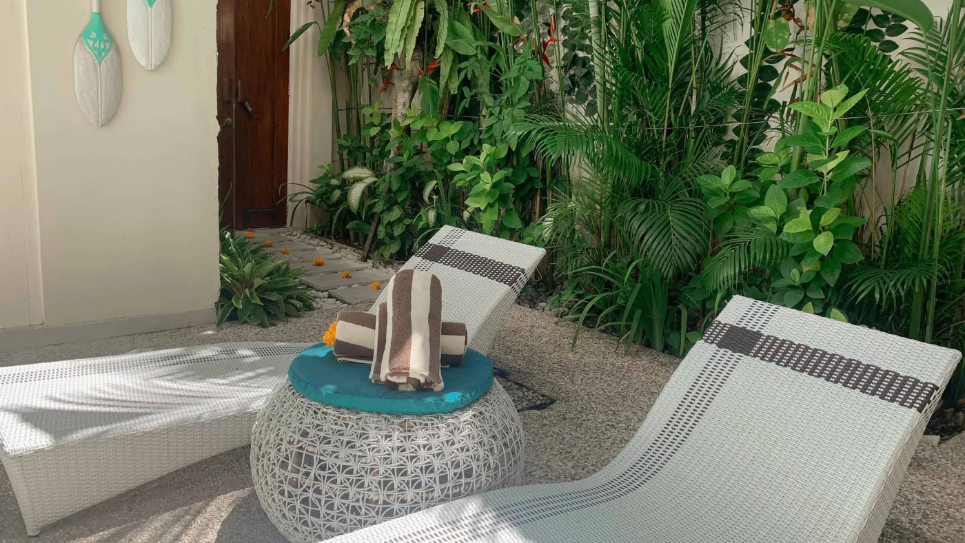 Serene private infinity pool in a modern Balinese villa courtyard, with white lounge chairs, tiled table, and tropical stone decor. - Bali Villas