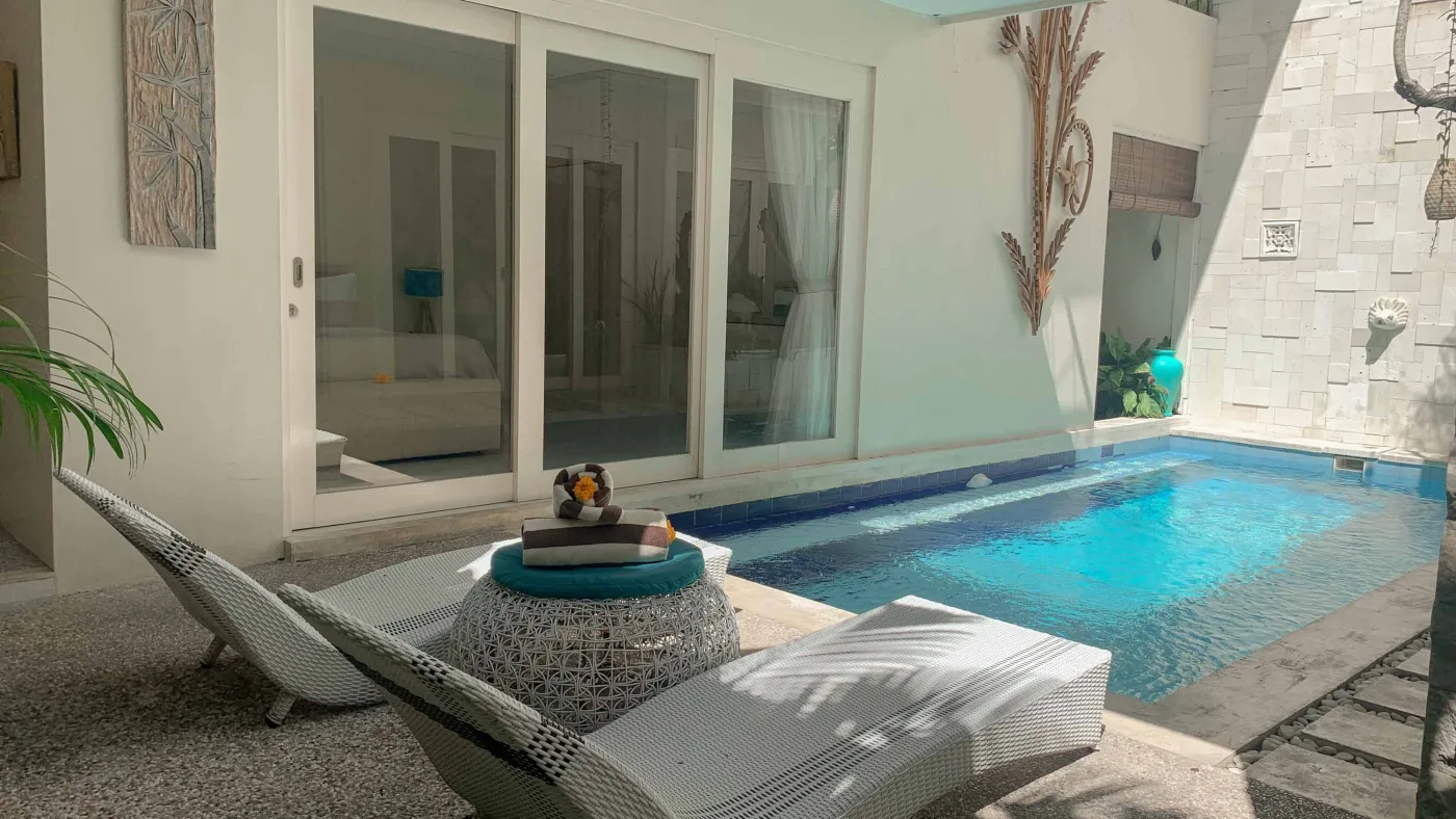 Serene private infinity pool in a modern Balinese villa courtyard, with white lounge chairs, tiled table, and tropical stone decor. - Bali Villas