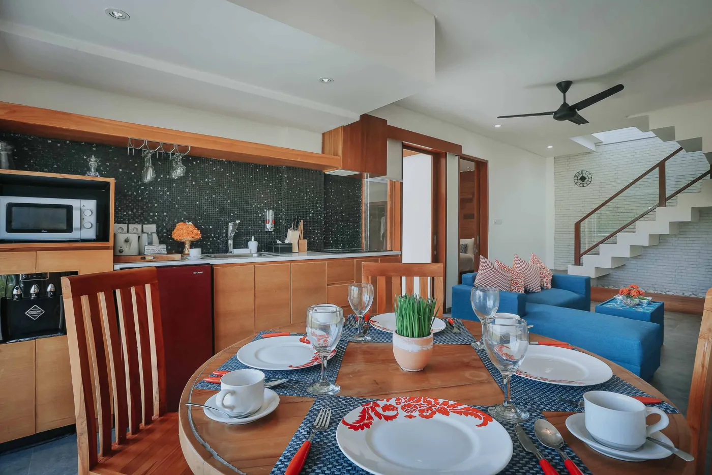 Luxurious Bali villa bedroom with king bed, wooden accents, wall mirror, and open balcony doors overlooking infinity pool and tropical palms. - Bali Villas