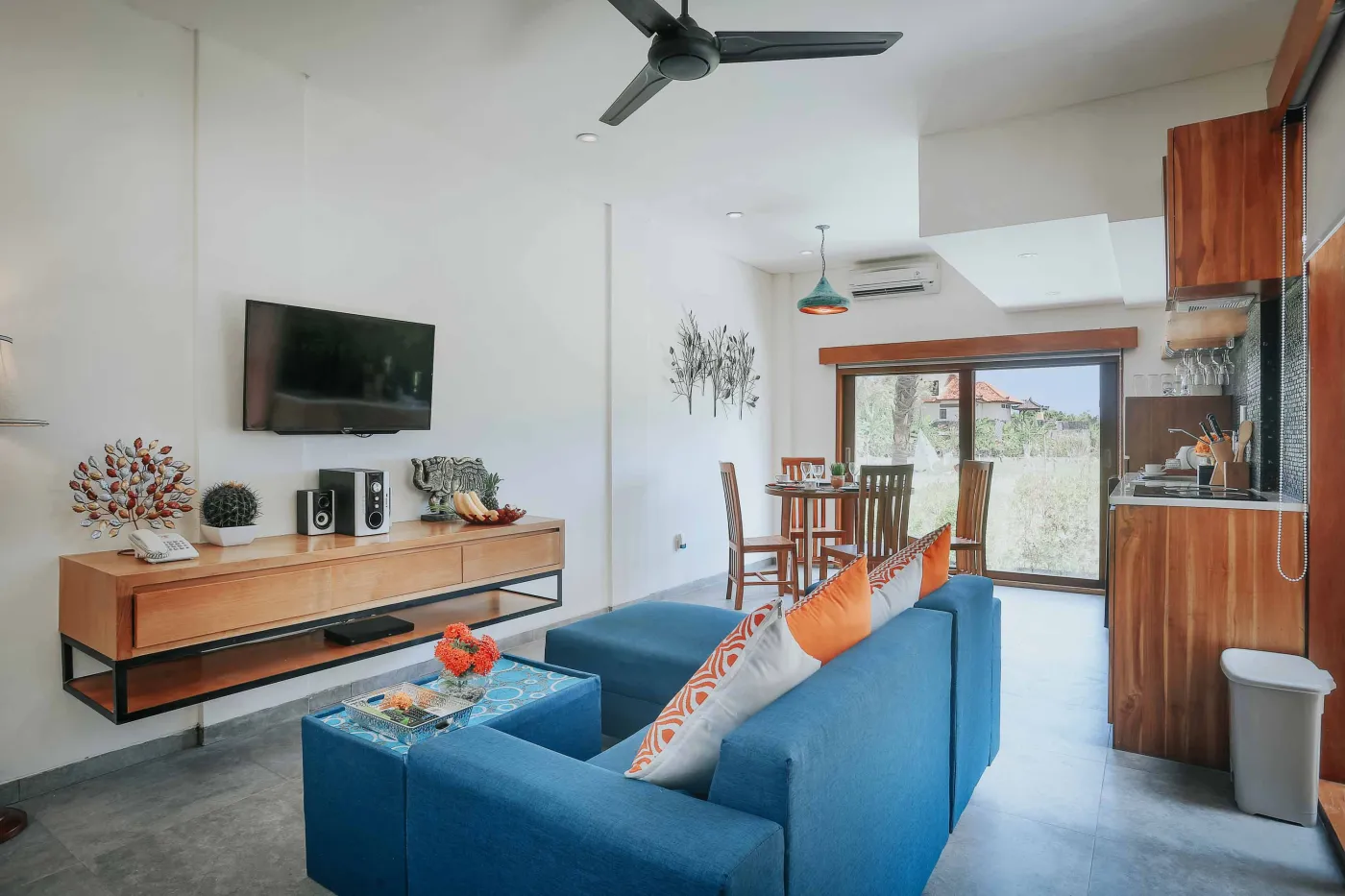 Luxurious Bali villa bedroom with king bed, wooden accents, wall mirror, and open balcony doors overlooking infinity pool and tropical palms. - Bali Villas