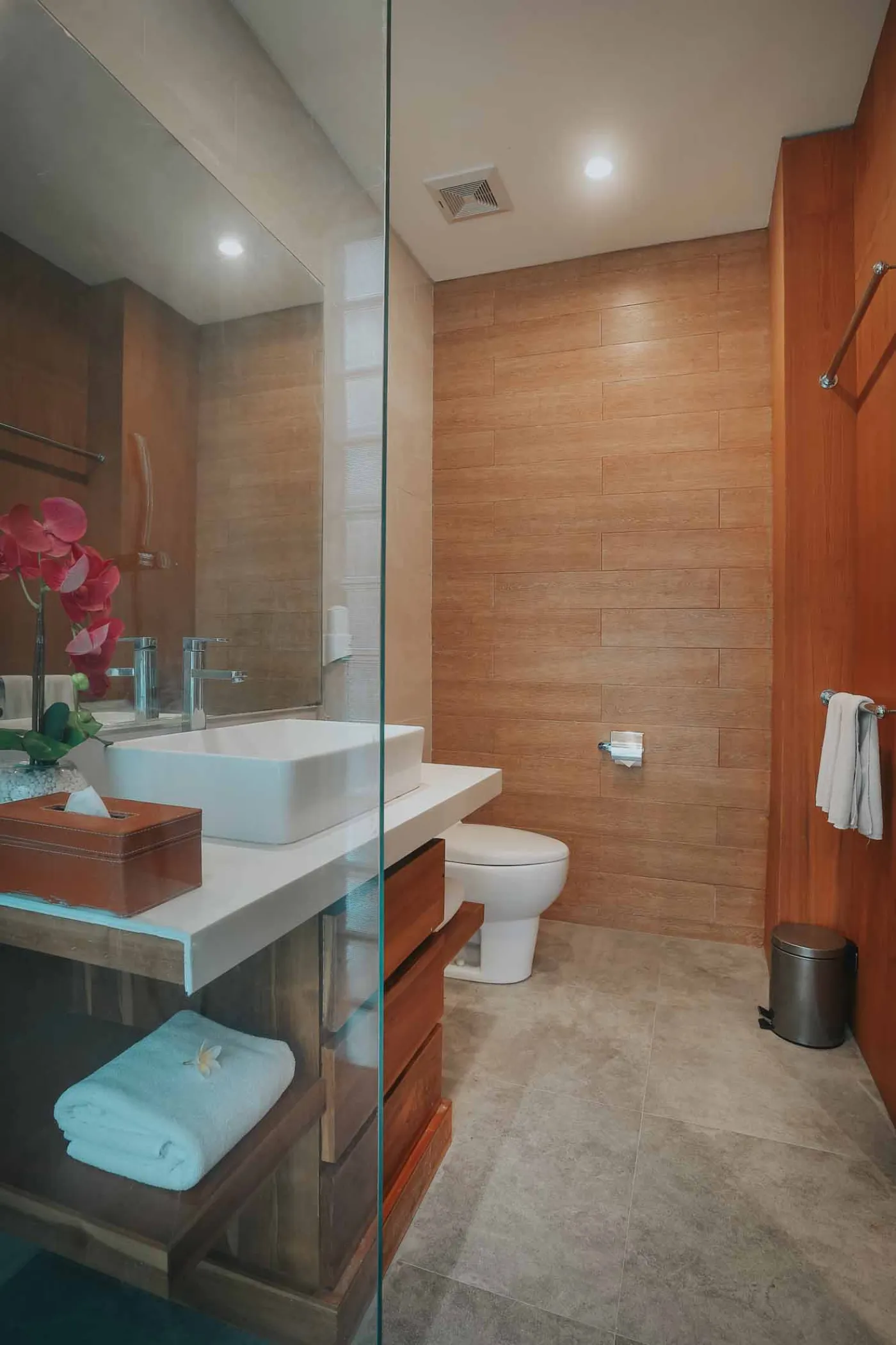 Luxurious Bali villa bedroom with king bed, wooden accents, wall mirror, and open balcony doors overlooking infinity pool and tropical palms. - Bali Villas