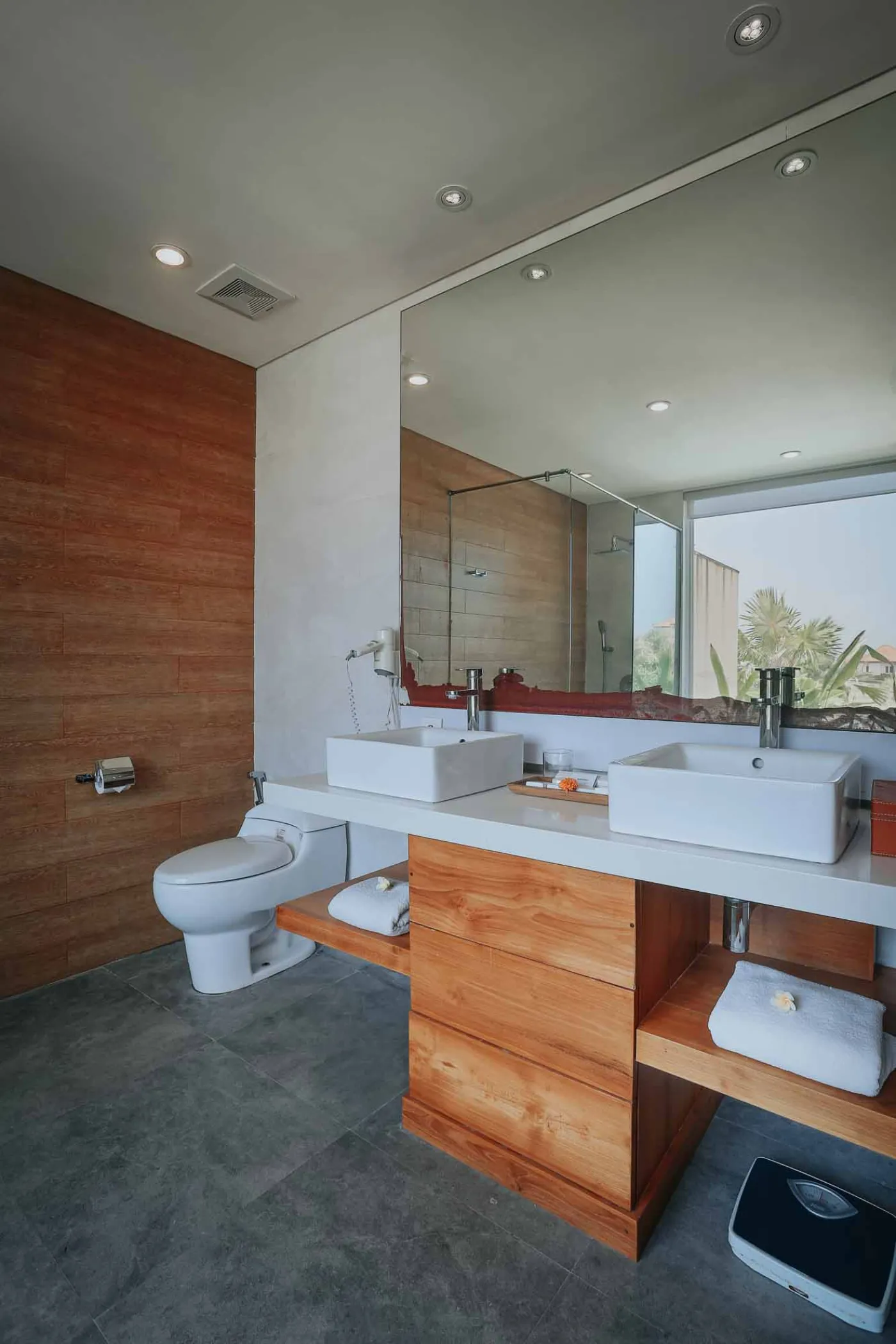 Luxurious Bali villa bedroom with king bed, wooden accents, wall mirror, and open balcony doors overlooking infinity pool and tropical palms. - Bali Villas