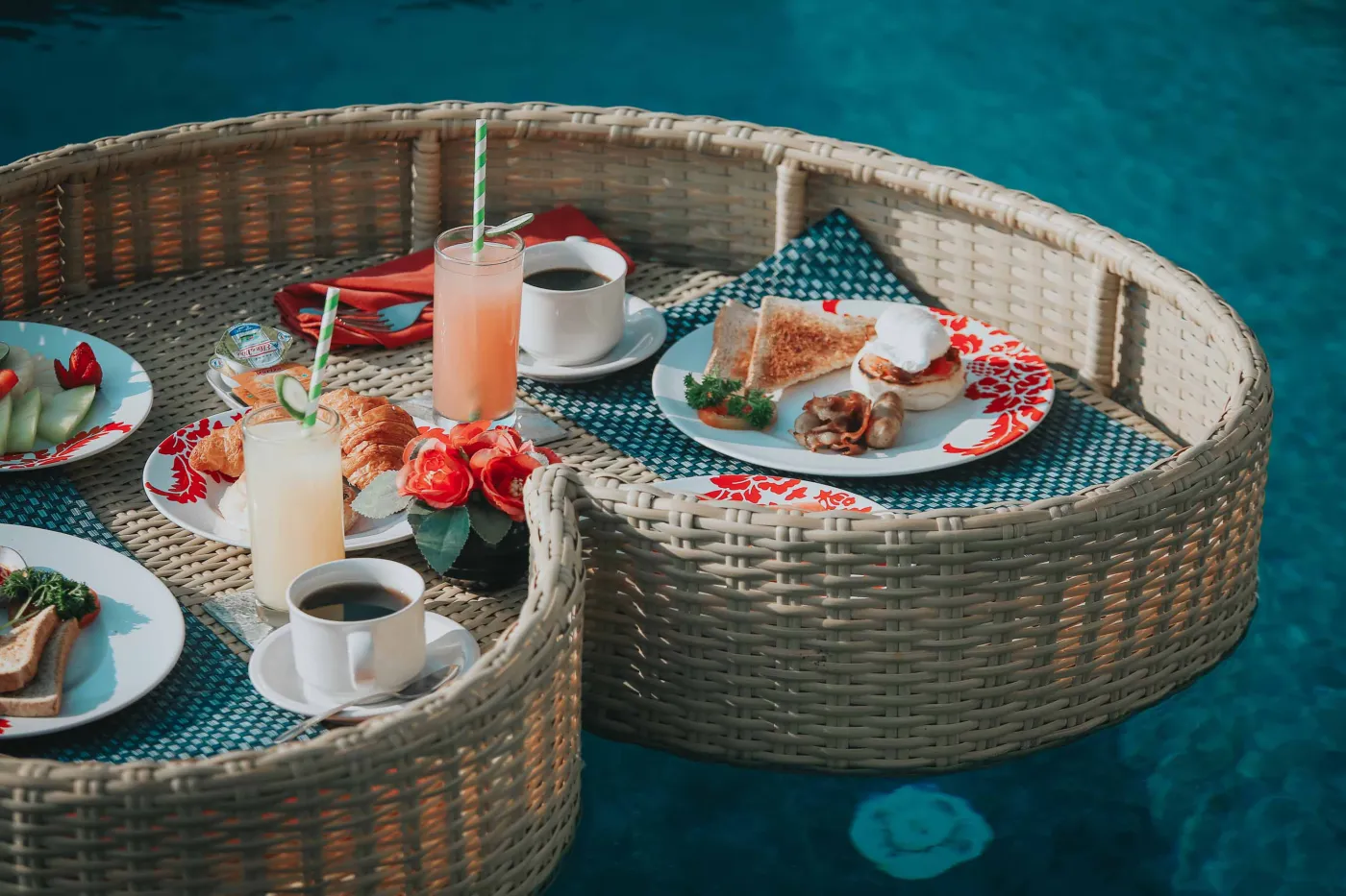 Luxurious Bali villa bedroom with king bed, wooden accents, wall mirror, and open balcony doors overlooking infinity pool and tropical palms. - Bali Villas