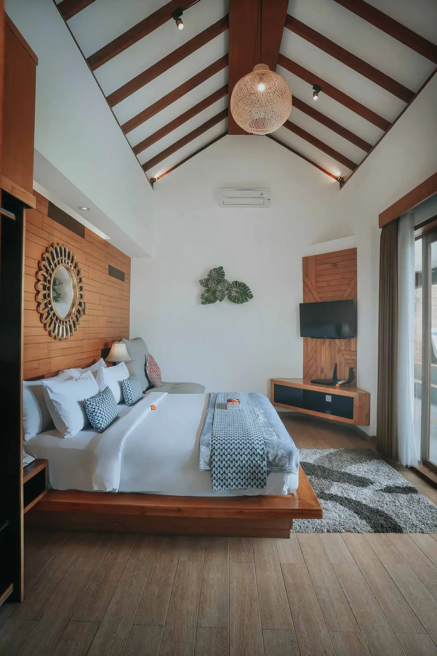 Modern luxury bathroom with freestanding white bathtub, glass shower enclosure, and floor-to-ceiling window overlooking tropical palm trees, pool, and villas. - Bali Villas