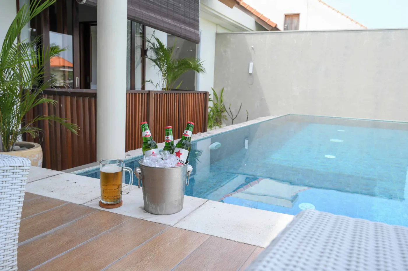 Modern luxury bathroom with freestanding white bathtub, glass shower enclosure, and floor-to-ceiling window overlooking tropical palm trees, pool, and villas. - Bali Villas