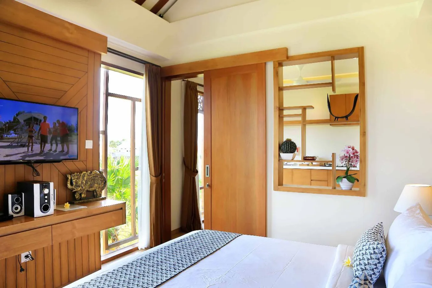 Spacious tropical villa bedroom with wooden walls, white king bed, en-suite bathtub, and wall-mounted TV. - Bali Villas