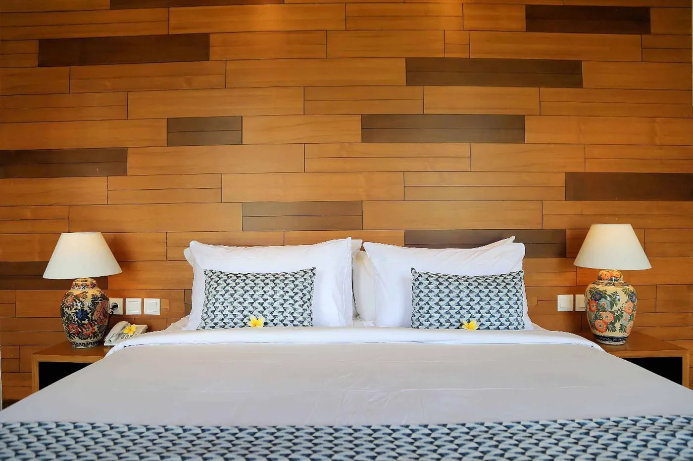 Spacious tropical villa bedroom with wooden walls, white king bed, en-suite bathtub, and wall-mounted TV. - Bali Villas